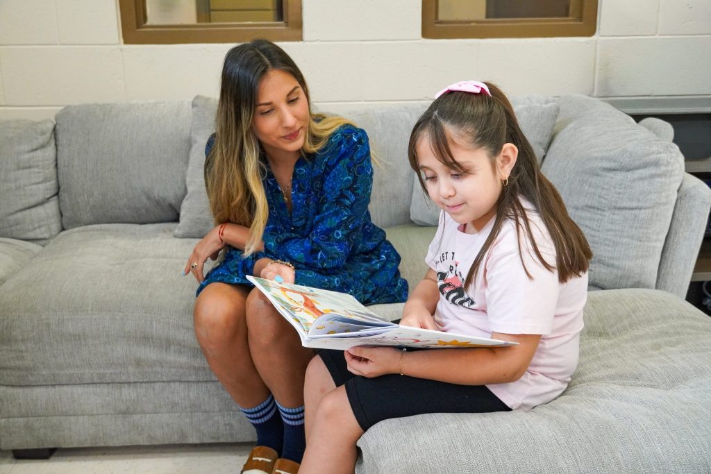 Immokalee Readers Program Coordinator, Natalia Areas, sitting with Analeya as she reads a book